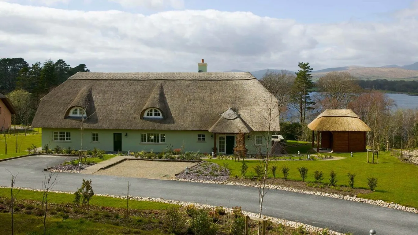 Cosy thatched-roof cottage with lush gardens, lake view, and a charming gazebo, ideal for a tranquil retreat in nature.