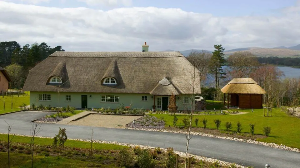 Cosy thatched-roof cottage with lush gardens, lake view, and a charming gazebo, ideal for a tranquil retreat in nature.