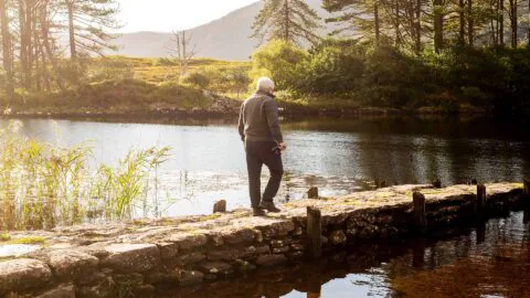 Guest enjoying a peaceful walk on a stone path by a scenic lake surrounded by lush trees at our tranquil hotel retreat.