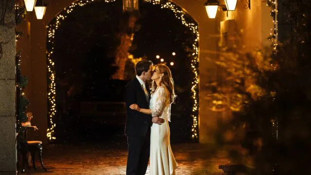 Romantic couple kissing under glowing fairy lights in elegant hotel courtyard, enhancing a special evening experience.