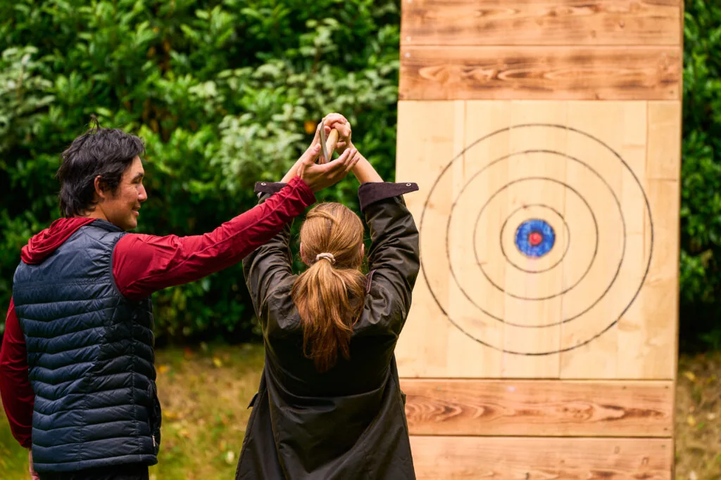 Axe throwing instructor showing a guest how to throw the axe at the target