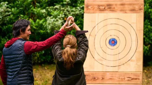 Axe throwing instructor showing a guest how to throw the axe at the target