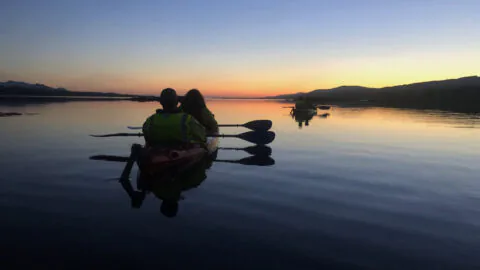 Serene sunset kayaking experience, guests paddle in calm waters with scenic mountain views, ideal for nature lovers.