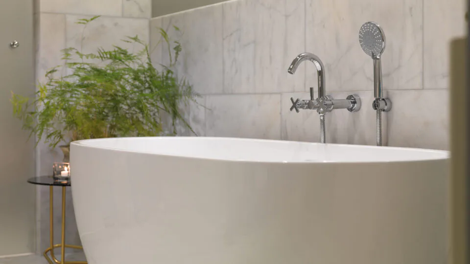 Luxurious marble bathroom with elegant free-standing tub, lush plant, and soothing ambience for a relaxing stay.