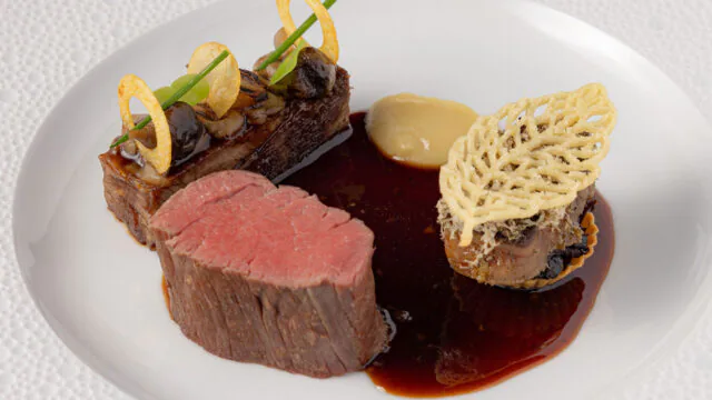 Exquisite fine dining dish with tender steak, rich sauce, and elegant garnishes at luxury hotel restaurant.