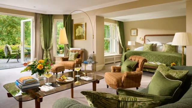 Spacious hotel suite with lush garden view, luxurious seating, cosy bed, open terrace, and elegant décor for relaxing stay.