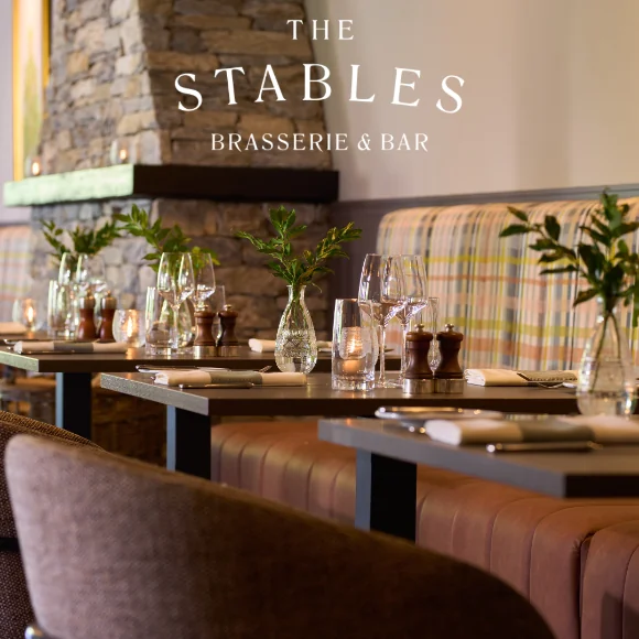Cosy brasserie with stone fireplace, candlelit tables, elegant glassware, and plush seating for a warm dining experience.