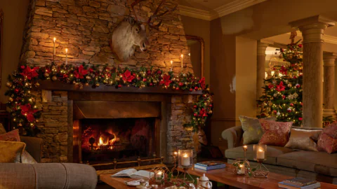 Cosy lounge with festive decor, roaring stone fireplace, plush seating, and a twinkling Christmas tree for a warm holiday stay.