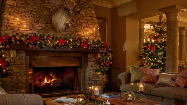 Cosy hotel lounge with roaring fireplace, elegant Christmas decor, soft sofas, and festive garlands, inviting ambience.