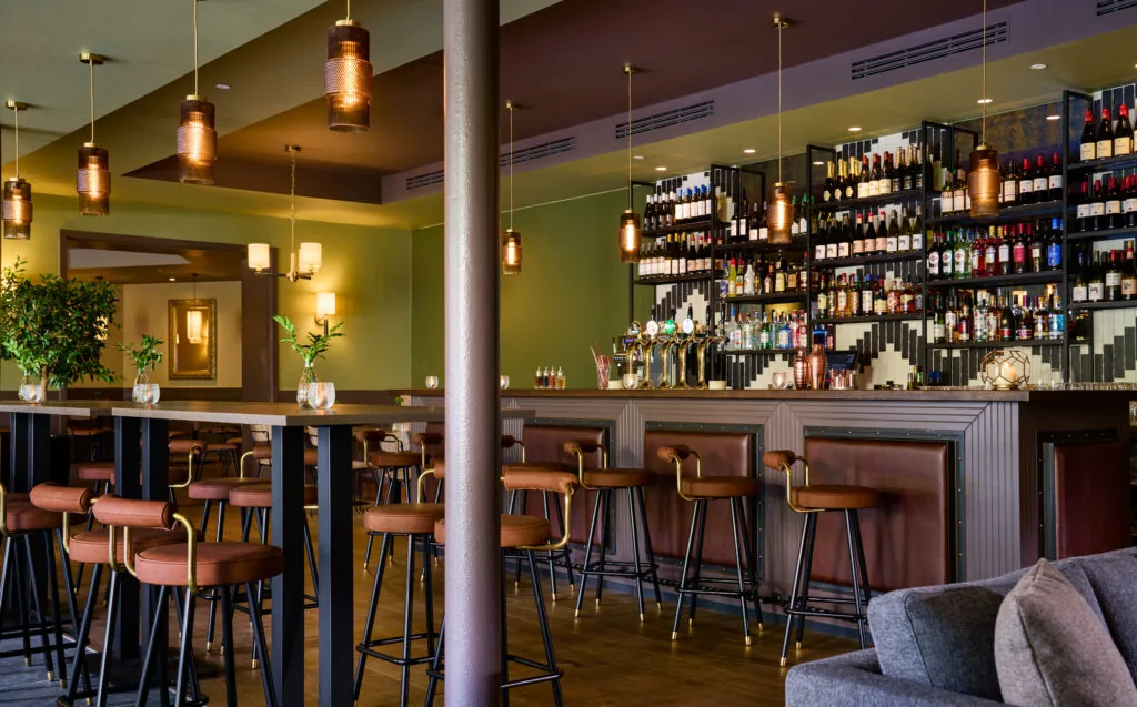 Stylish hotel bar with warm lighting, plush leather stools, and a wide selection of spirits, offering a welcoming ambience.