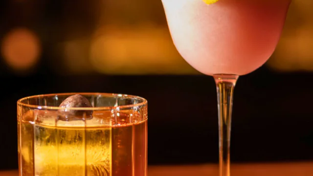Two elegant cocktails on a polished wooden bar, illuminated warmly, inviting a relaxing hotel lounge experience.