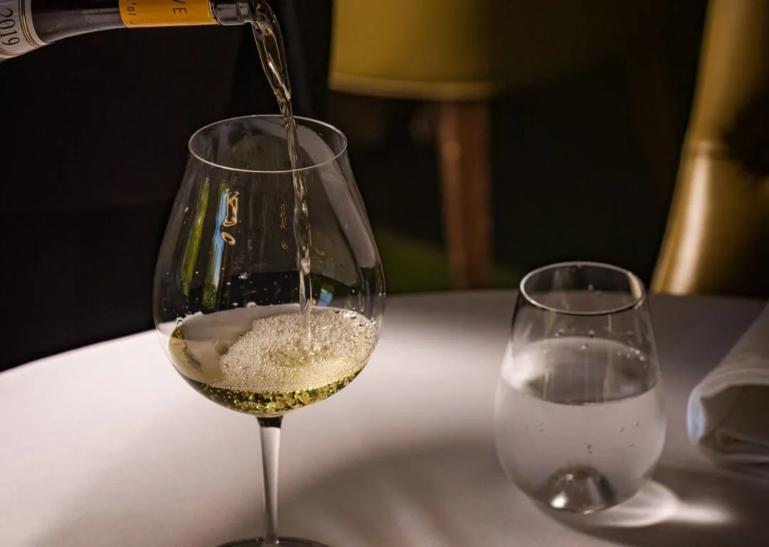 A bottle of white wine is being poured into a wine glass on a white tablecloth next to a glass of water.