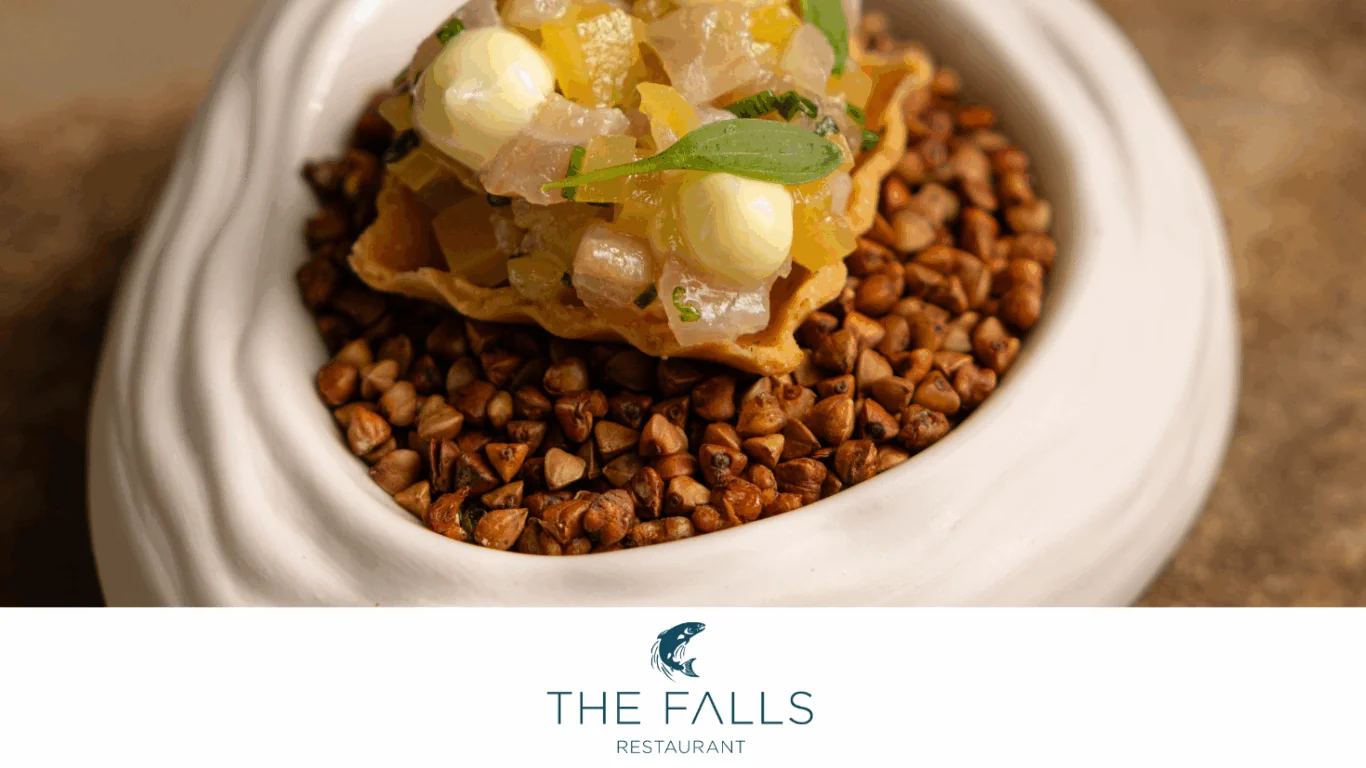 A gourmet appetizer with diced vegetables and sauce on a crispy shell, served on a bed of grains in a white bowl. Logo below reads: 