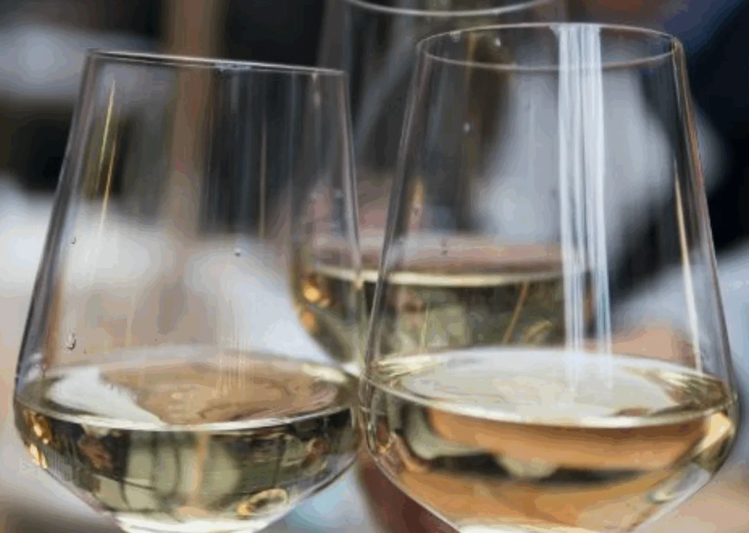 Three people clinking glasses of white wine in a toast, with a blurred background of other people.