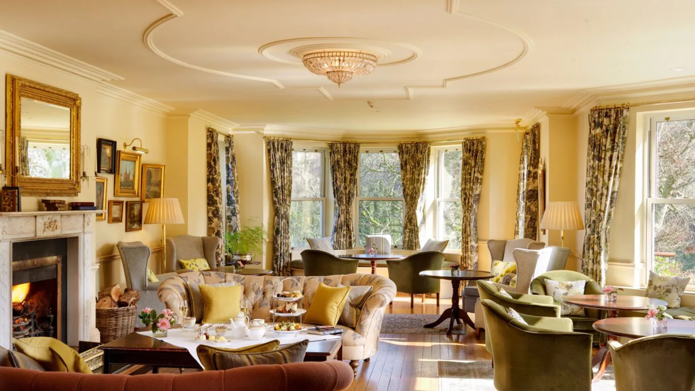 Charming hotel lounge with plush seating, fireplace, and afternoon tea. Elegant decor, large windows, and natural light.