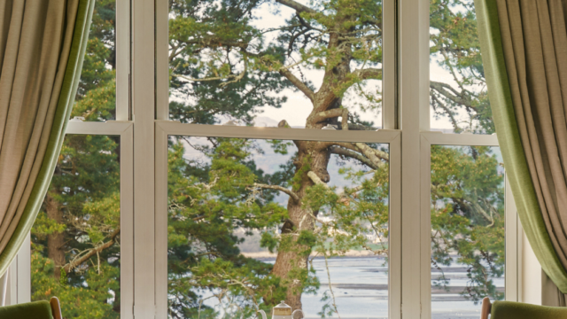 Cosy seating area with scenic bay view, elegant tea set on wooden table, green chairs, luxurious curtains in serene hotel room.