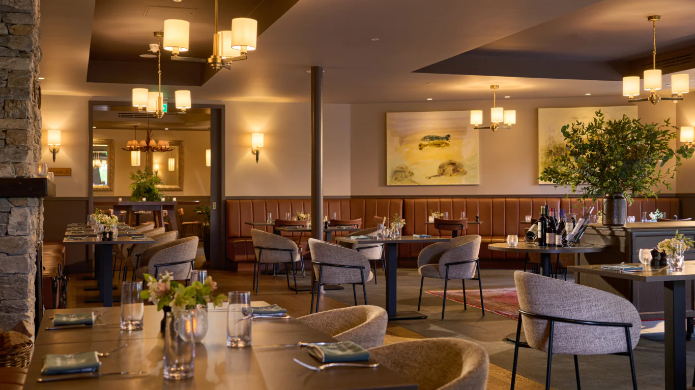 Elegant hotel dining room with cosy seating, warm lighting, modern decor, and lush greenery for a relaxing dining experience.