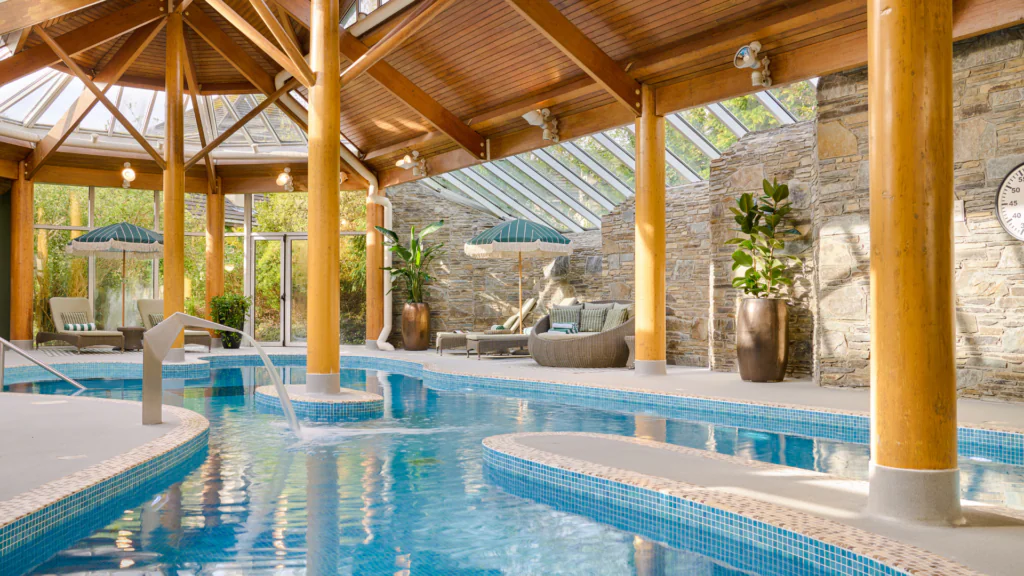 Relax in the serene indoor pool with wooden beams and loungers at a stylish hotel, perfect for a refreshing getaway.