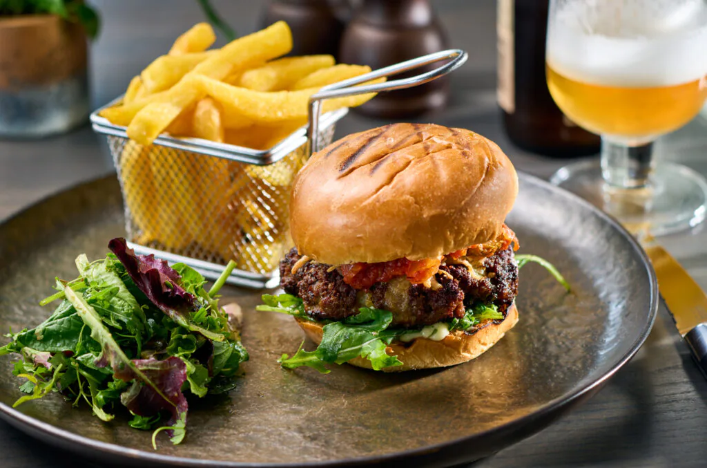 Savour a gourmet burger with crispy chips and fresh salad at our hotel's restaurant, perfect for relaxing dining.