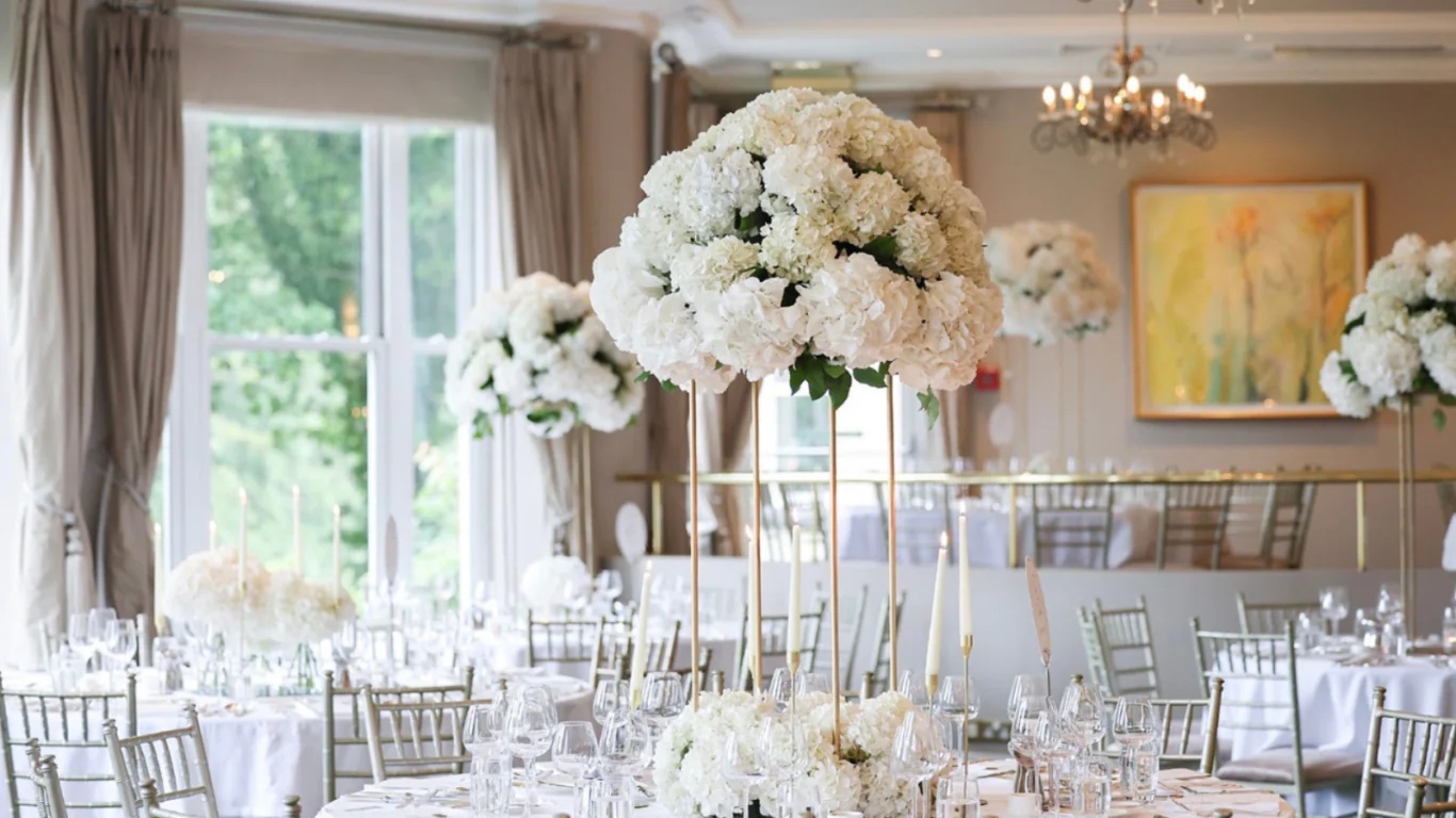 Elegant hotel ballroom with white floral centrepieces, chandeliers, and large windows offering scenic views, perfect for events.
