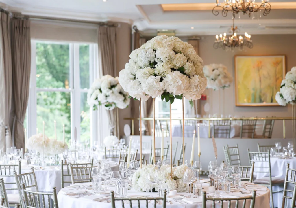 Elegant hotel banquet hall with large floral centrepieces, chandeliers, and soft natural light for a serene dining experience.