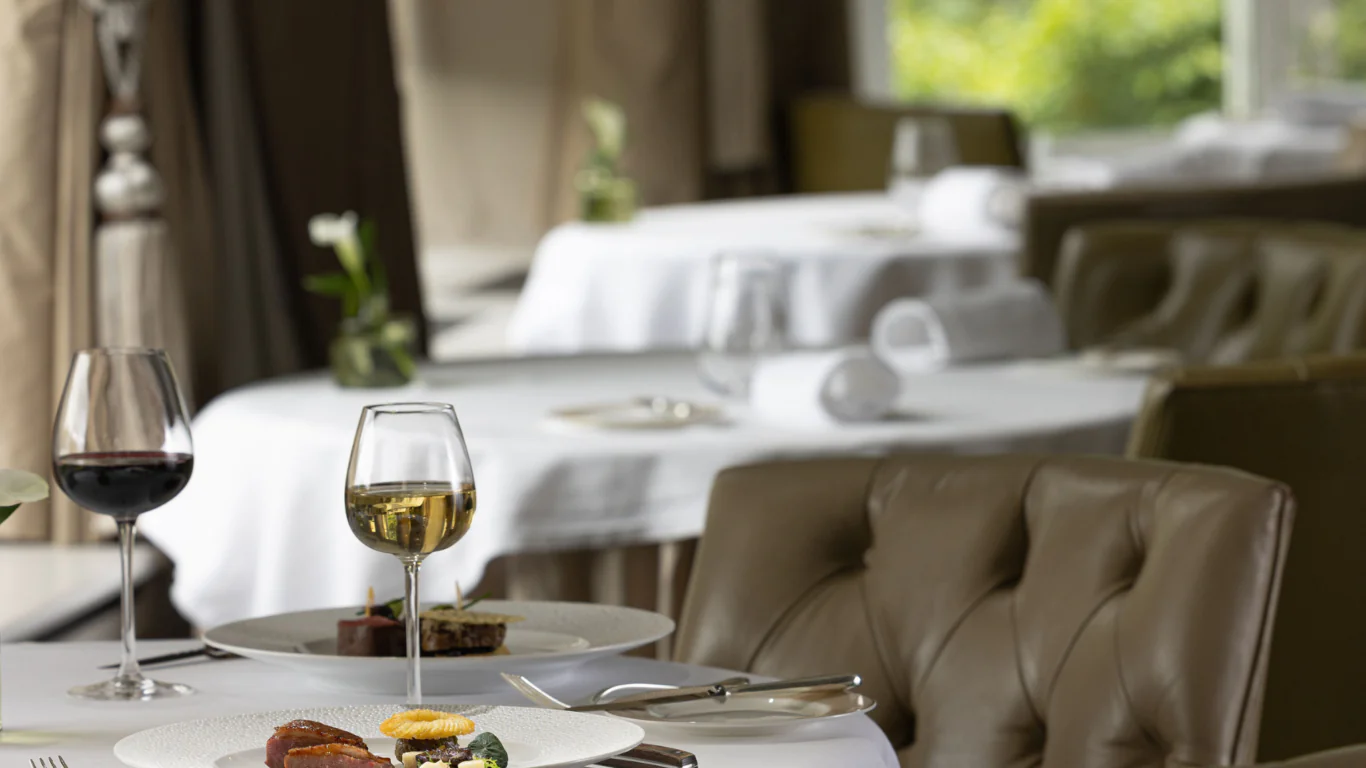 Elegant dining room with plush chairs, gourmet dishes, and wine glasses set on white tablecloths, offering a refined experience.