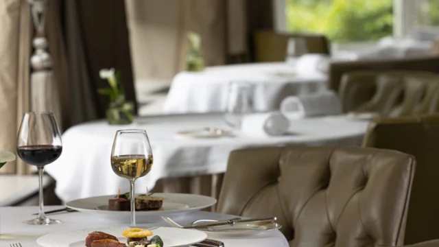 Elegant dining room with plush chairs, gourmet dishes, and wine glasses set on white tablecloths, offering a refined experience.