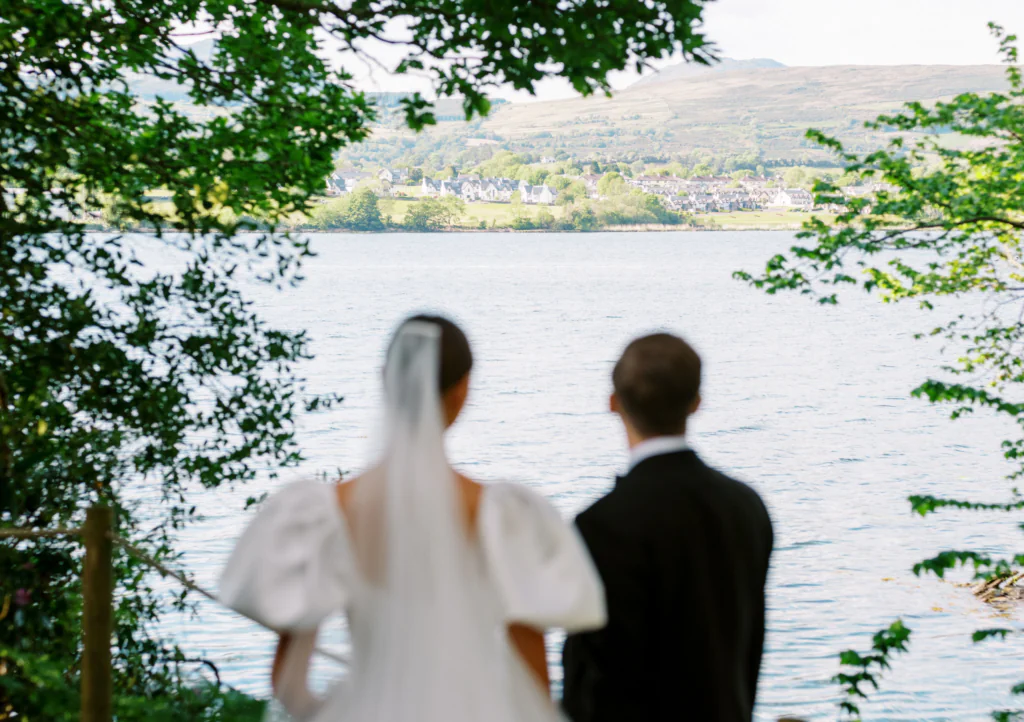 Newlyweds enjoy a serene lake view with green hills, perfect for romantic getaways and weddings at our scenic hotel.