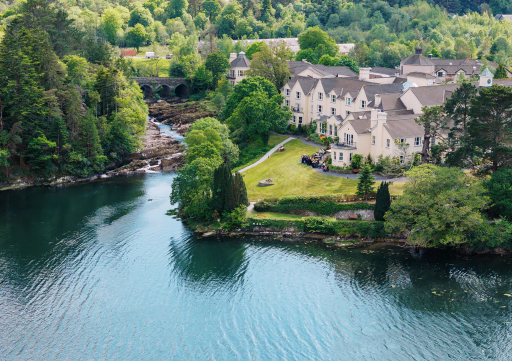 Guests enjoy riverside views at a cosy hotel with lush gardens, nestled by tranquil waters and scenic bridge in serene countryside.