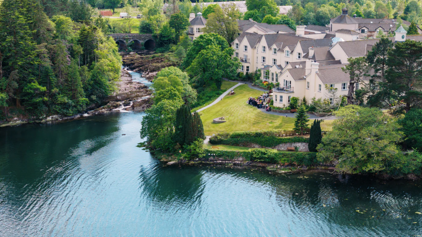 Guests enjoy riverside views at a cosy hotel with lush gardens, nestled by tranquil waters and scenic bridge in serene countryside.