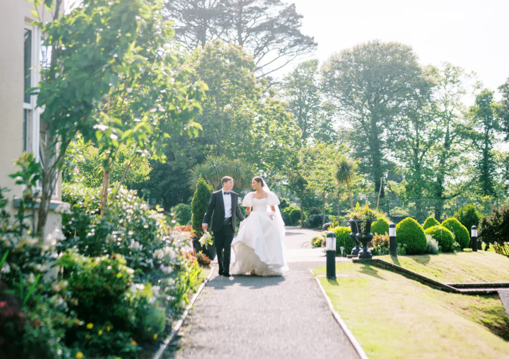 Newlyweds stroll through lush hotel gardens, surrounded by vibrant flowers and scenic views, ideal for romantic getaways.