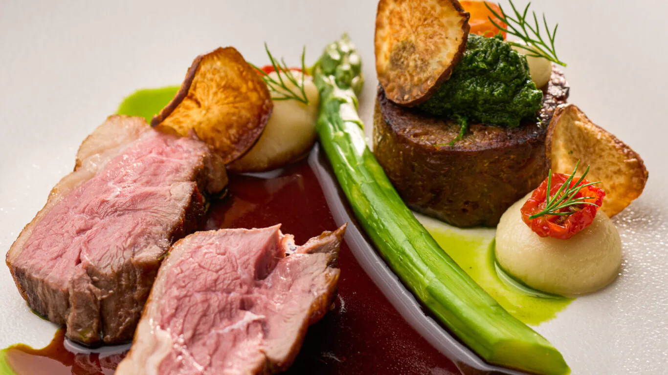Gourmet dish with lamb slices, vegetables, and sauce, showcasing fine dining at our luxury hotel restaurant.