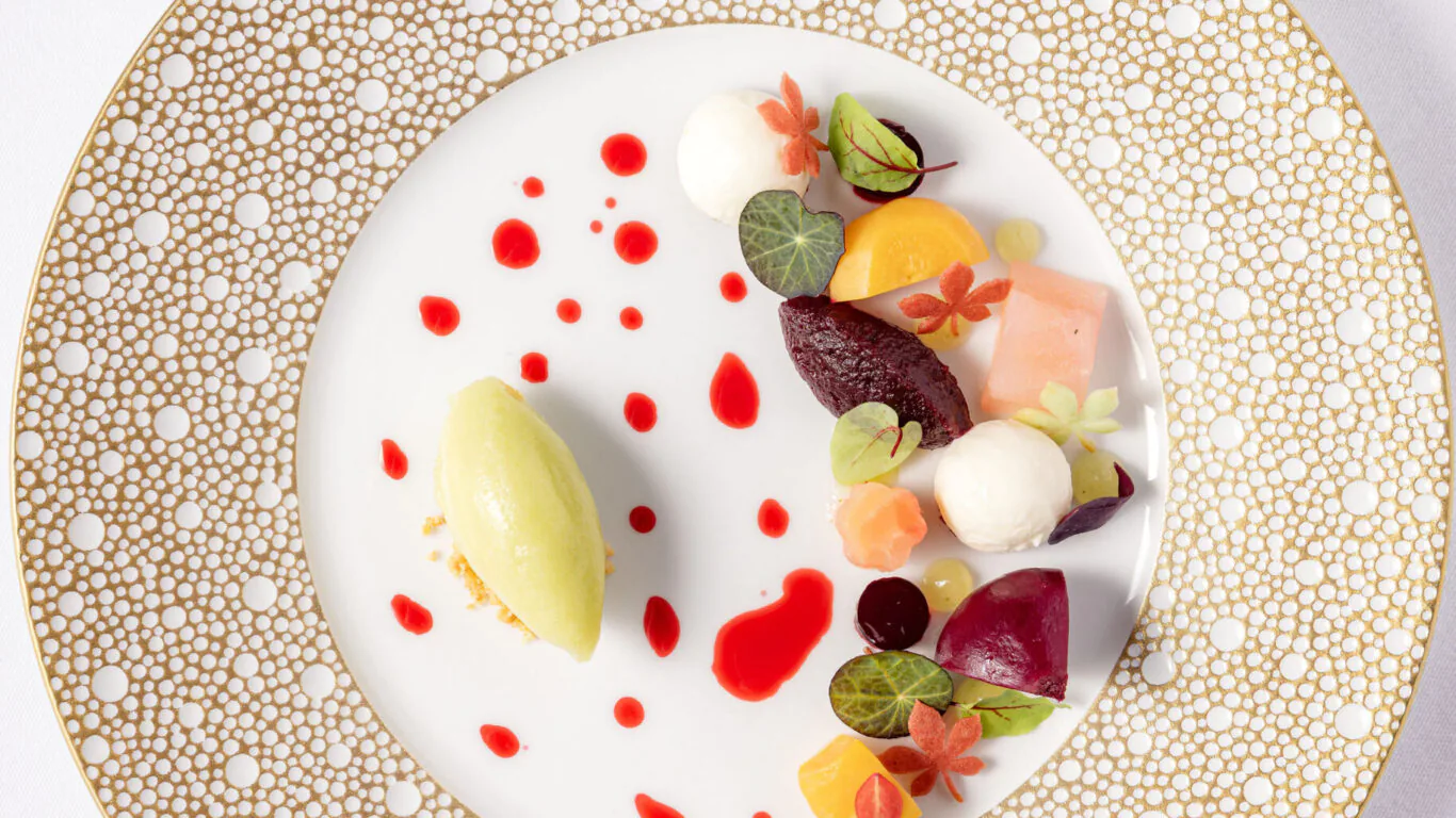 Exquisite gourmet dessert with colourful garnishes on elegant white and gold plate, showcasing fine dining experience.