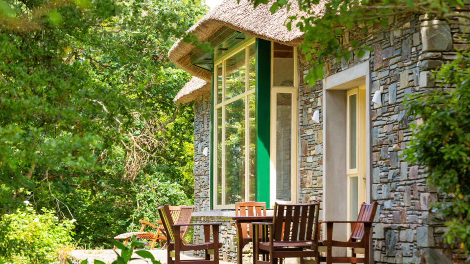 Cosy stone cottage patio with wooden furniture, surrounded by lush greenery for a tranquil retreat experience.