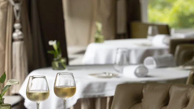 Elegant hotel dining room with plush seating, wine glasses on a table, and garden views, offering a cosy and refined dining experience.