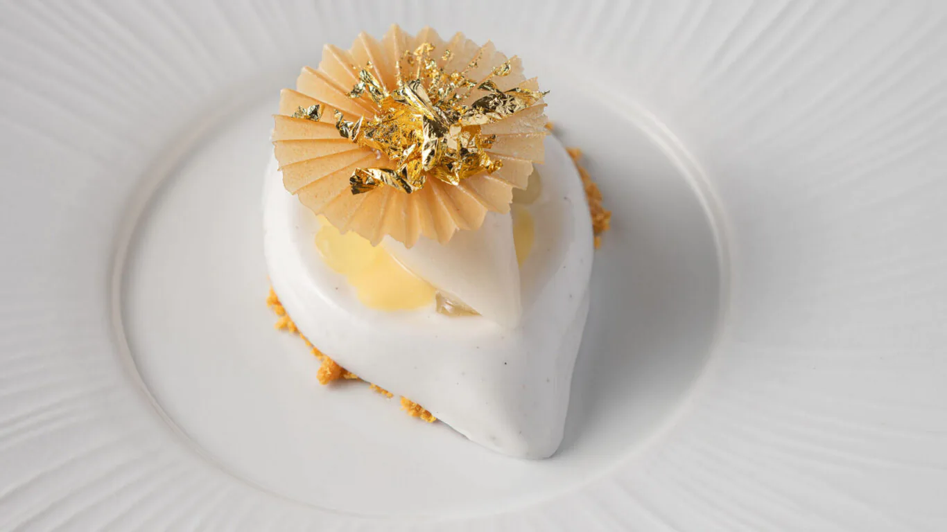 Elegant dessert with creamy layers and gold leaf on a textured white plate, offering a luxurious dining experience.