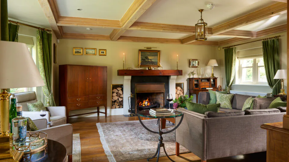 Cosy hotel lounge with fireplace, elegant sofas, vibrant green curtains, and soft lighting, offering a warm, inviting atmosphere.