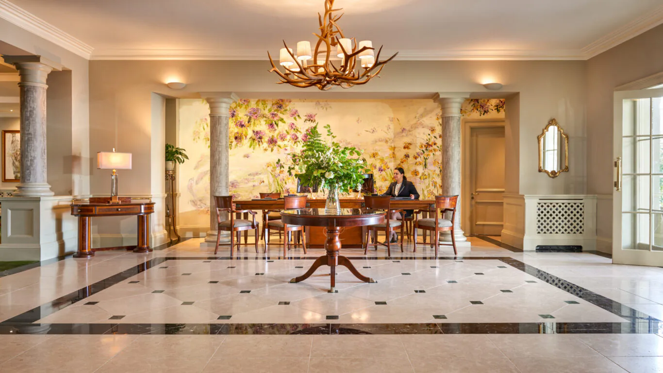 Elegant hotel lobby with grand chandelier, marble flooring, vibrant mural, and welcoming seating area.