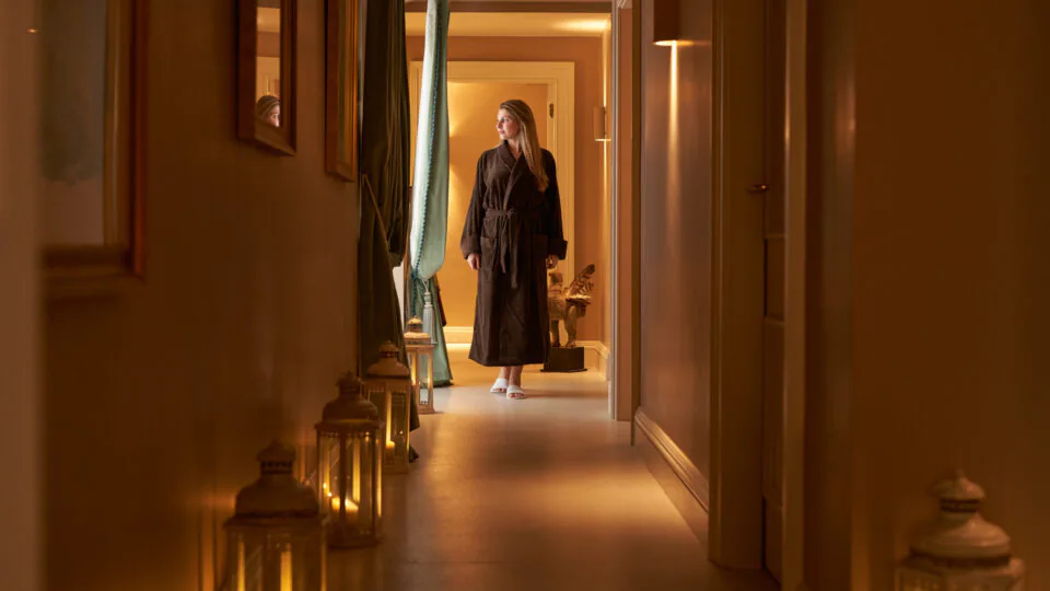 Guest in spa robe walking through candlelit hotel corridor for a relaxing retreat experience. Warm, inviting ambiance.